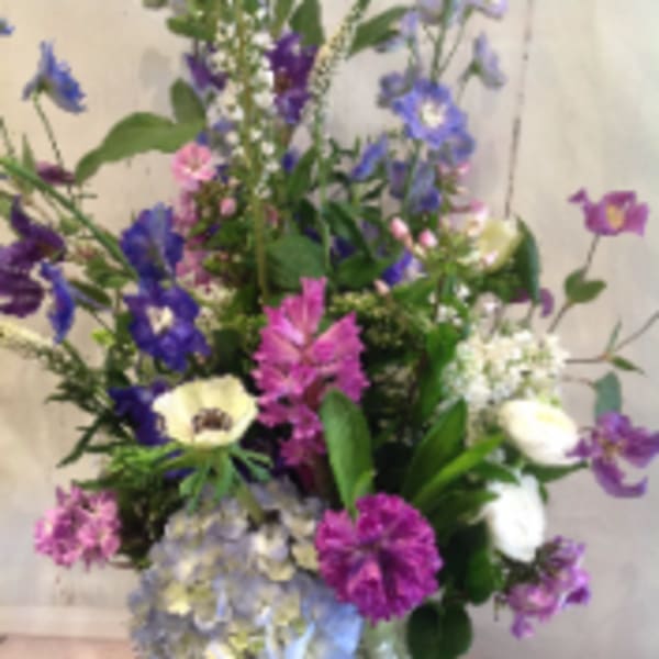 Tall mixed bouquet of purple, blue, pink, and white flowers in a clear glass vase