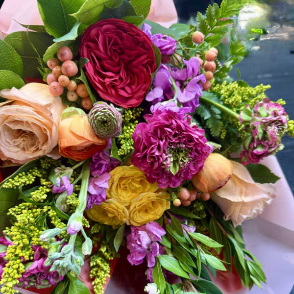 Bright hand-tied bouquet of pink, yellow, peach, and purple blooms wrapped in pastel paper