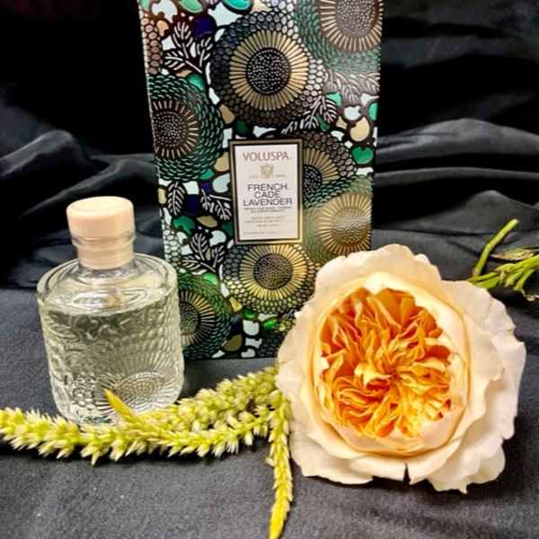 Perfume bottle, floral candle box, and a peach rose on dark fabric