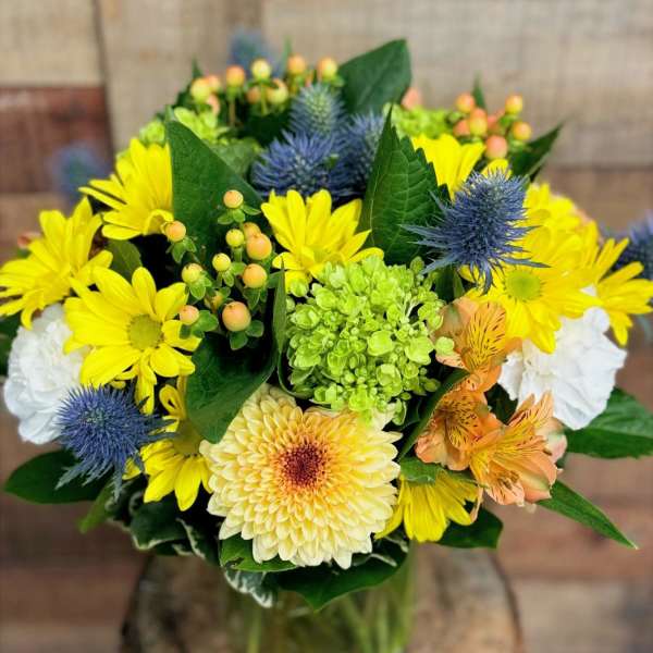 Bouquet of yellow daisies and blue thistle in a glass vase
