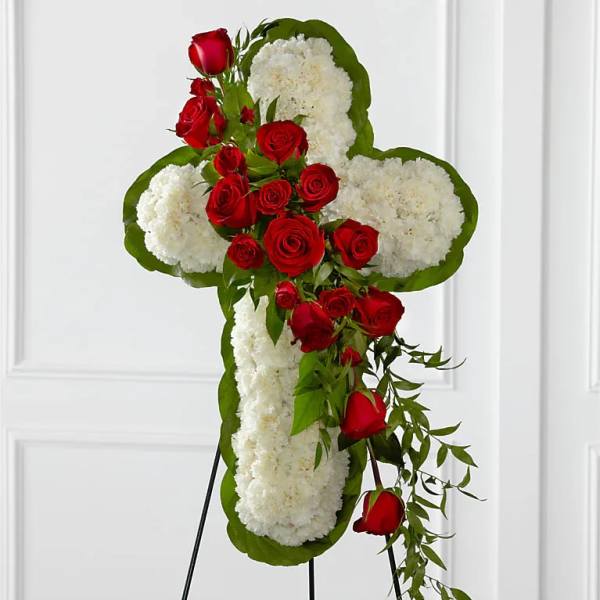 Cross-shaped floral tribute with red roses and white flowers on a stand