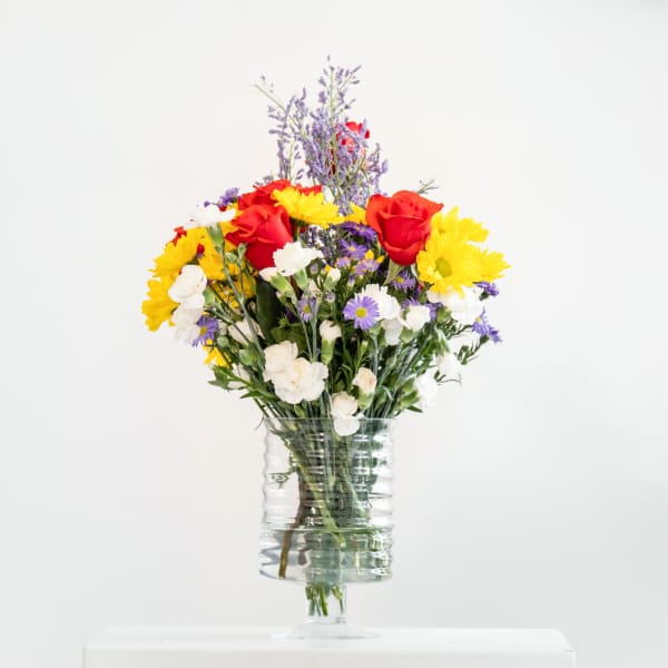 Mixed bouquet of red roses, yellow daisies, and white flowers in a clear glass vase
