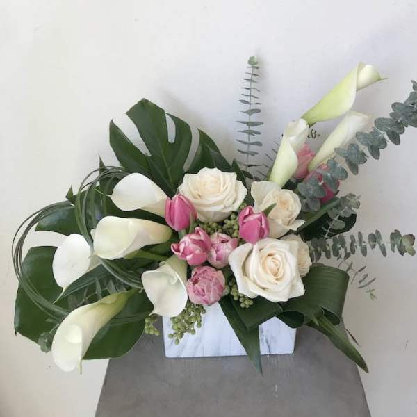 White calla lilies and roses with pink tulips in a white vase