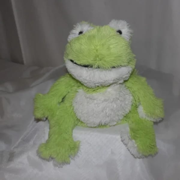 Green and white plush frog toy sitting on a bed