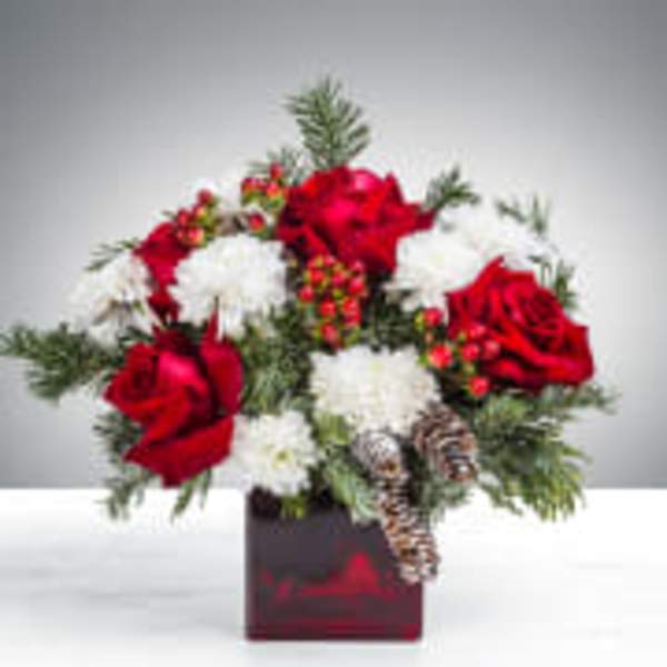 Red and white floral arrangement in a dark square vase with pinecones