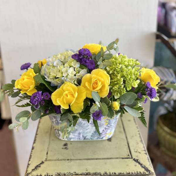 Yellow roses and purple flowers in a patterned rectangular container