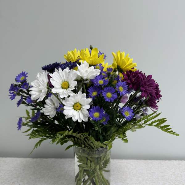 Mixed bouquet of daisies and purple flowers in a clear glass vase