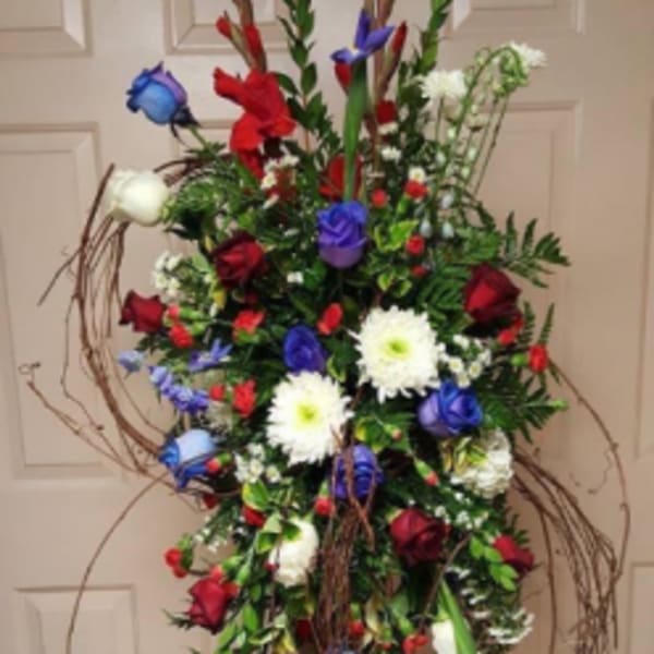 Tall standing floral spray with red, white, and blue flowers on a wire easel
