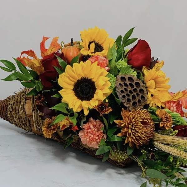 Autumn bouquet with sunflowers, red roses, and orange blooms in a woven basket