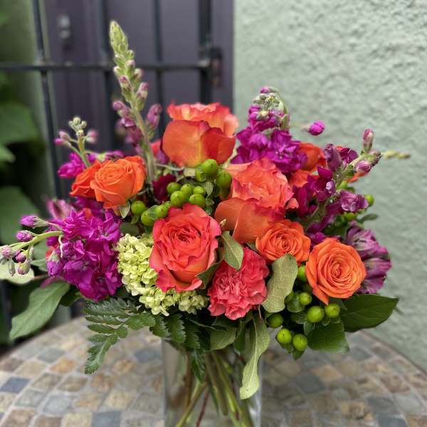 Bright arrangement of orange roses and pink flowers in a clear glass vase on a mosaic table