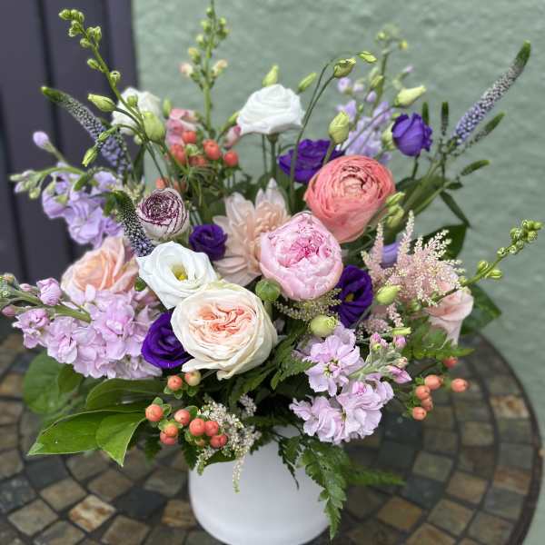 Pastel pink and white flower arrangement with purple accents in a white vase on a mosaic table.