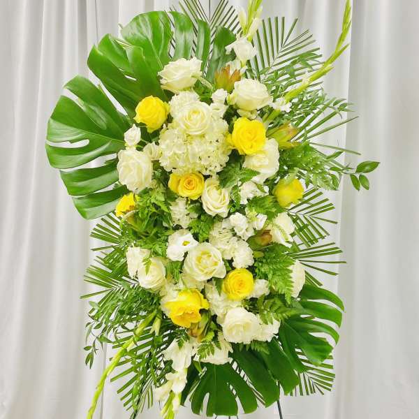Tall floral standing spray with white and yellow roses and tropical leaves