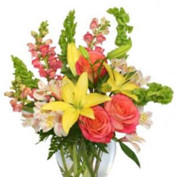 Bouquet of yellow lilies, pink roses, and snapdragons in a glass vase
