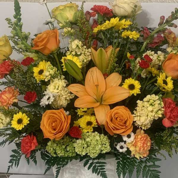 Mixed bouquet of orange roses, lilies, and yellow daisies in a white vase