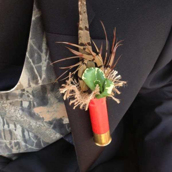 Small boutonniere with a red shotgun shell and green accent on dark fabric