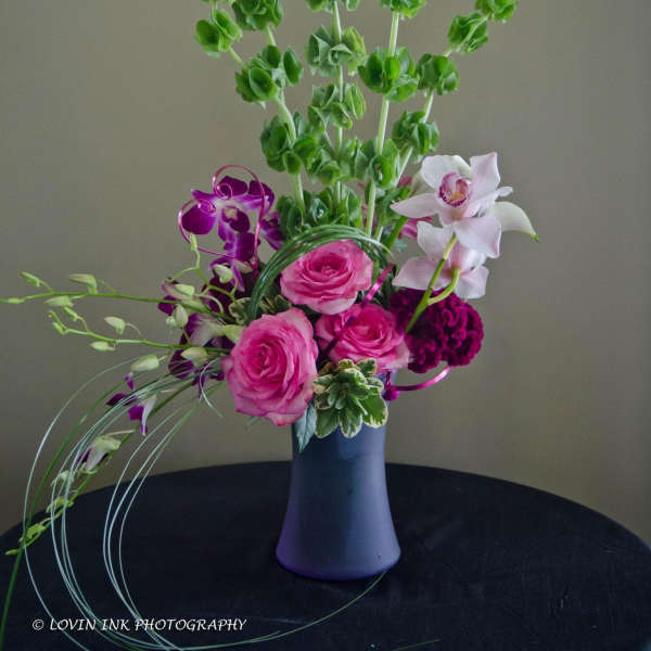 Tall bouquet with pink roses, purple orchids, and white orchids in a purple vase
