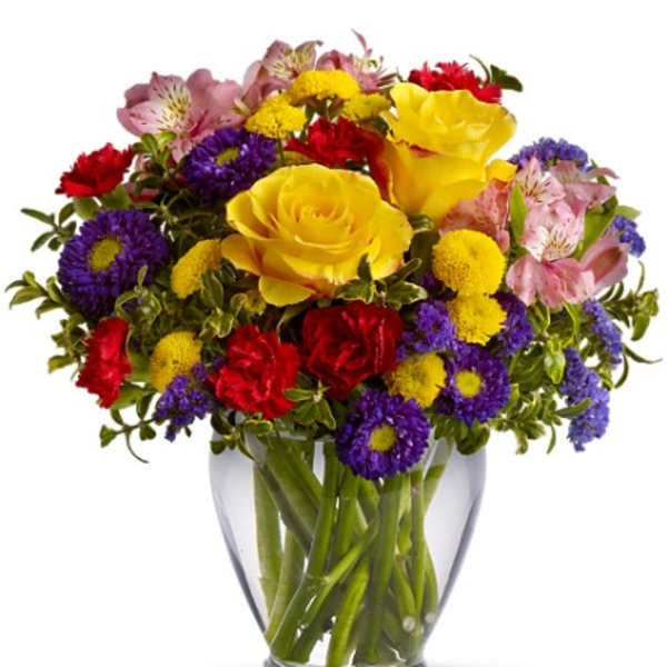 Mixed bouquet of yellow roses, red carnations, and purple daisies in a glass vase
