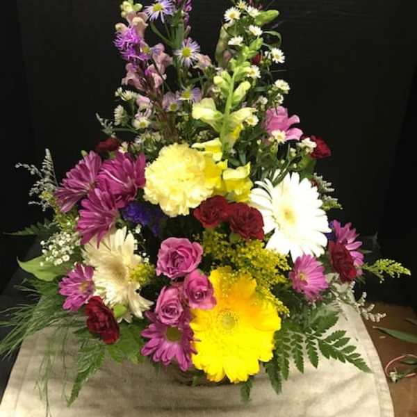 Tall mixed flower arrangement with daisies, roses, and lilies in bright colors