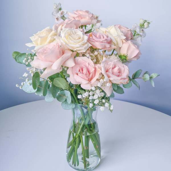 Pink and white roses in a clear glass vase with eucalyptus