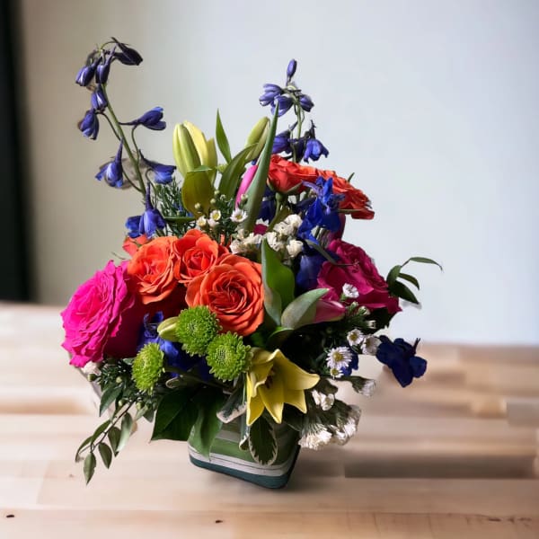 Colorful mixed bouquet in a square vase with roses and lilies