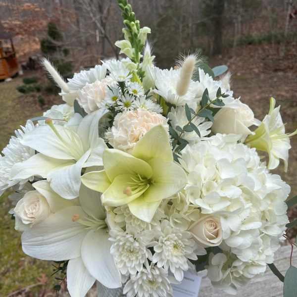White floral bouquet in a glass vase with lilies, hydrangeas, and roses
