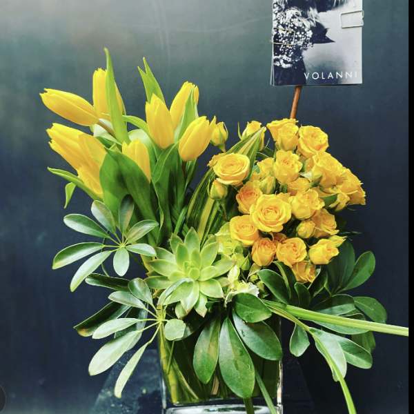 Yellow tulips and roses in a glass vase with green foliage