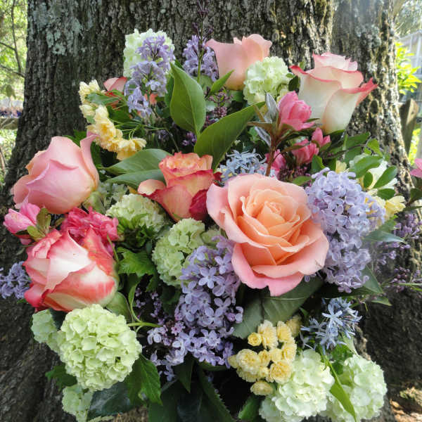 Bouquet of pink roses, lilac blooms, and pale green hydrangeas in a glass vase