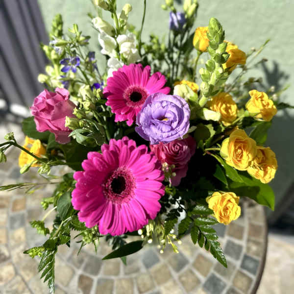 Bright bouquet with hot pink gerbera daisies, yellow spray roses, purple lisianthus, and white snapdragons