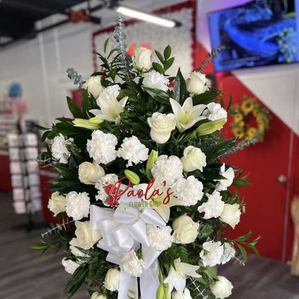 White roses and lilies arranged on a standing spray with a white ribbon