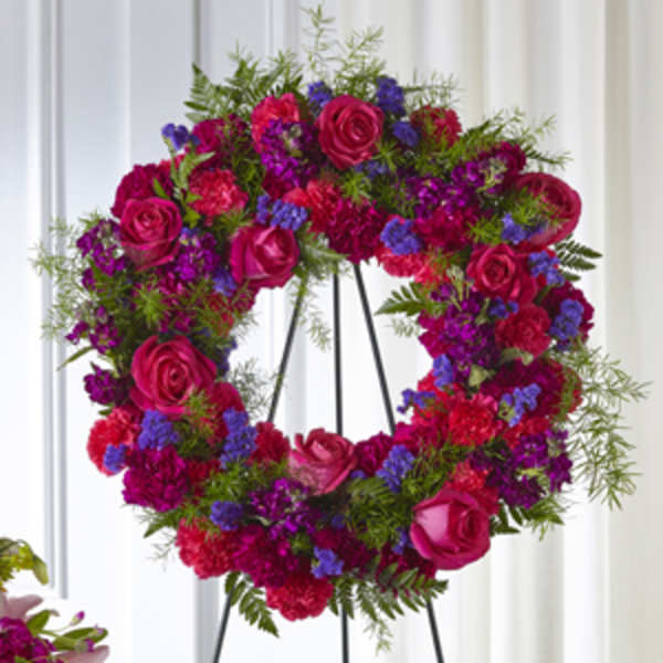 Heart-shaped floral wreath with pink roses and purple flowers on a stand
