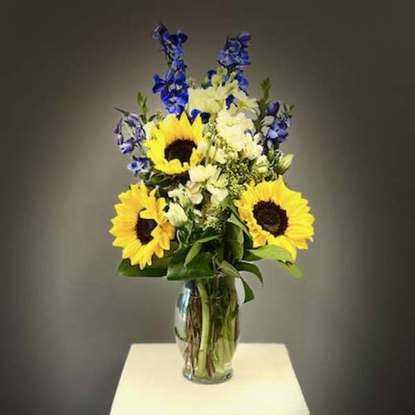 Sunflowers and blue flowers arranged in a clear glass vase