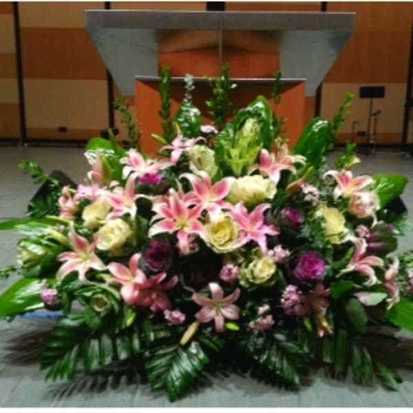 Large mixed arrangement of pink lilies and cream blooms displayed in front of a podium.