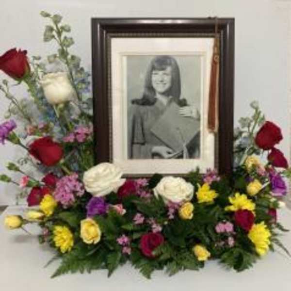 Sympathy floral arrangement around a framed portrait with red, white, and yellow flowers