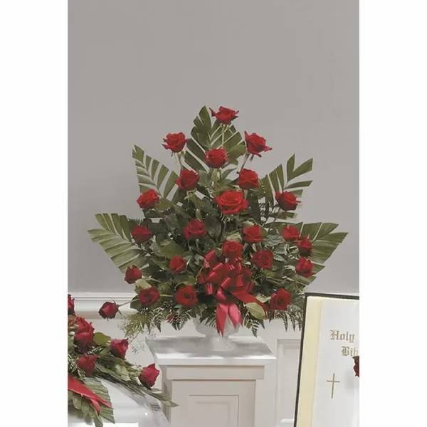 Tall arrangement of red roses with broad tropical leaves and a red ribbon