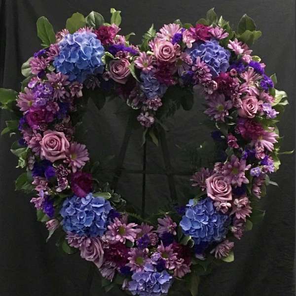 Heart-shaped floral wreath with blue hydrangeas, pink roses, and purple daisies
