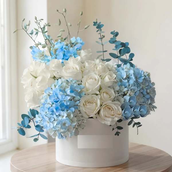 White and blue floral arrangement in a round white box