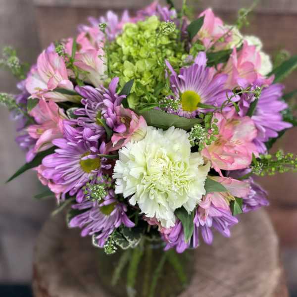 Bouquet of purple and pink flowers with a white carnation in a glass vase