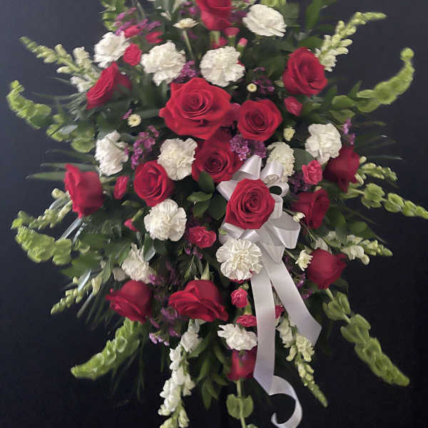 Red roses and white carnations in a standing spray with a white ribbon