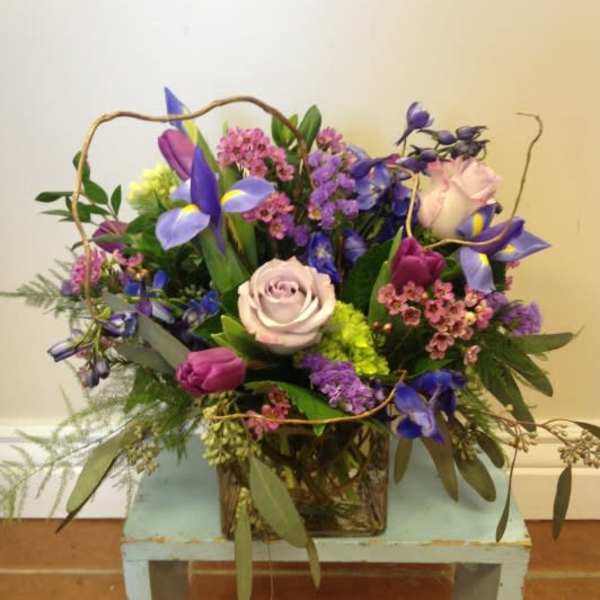 Mixed bouquet of purple, pink, and pale roses in a square container