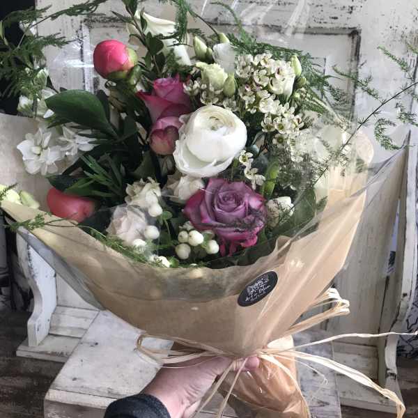 Hand-tied bouquet of pink, white, and purple flowers wrapped in tan paper