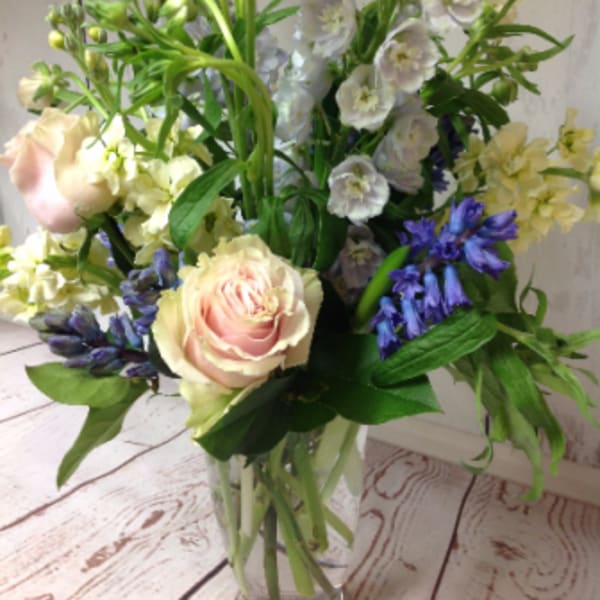 Tall mixed bouquet of pale pink roses and soft blue flowers in a clear glass vase