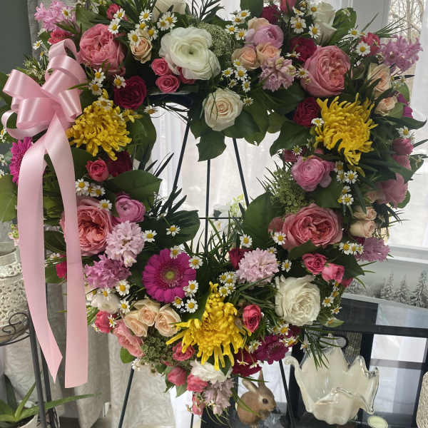 Heart-shaped floral wreath with pink, white, and yellow flowers on an easel