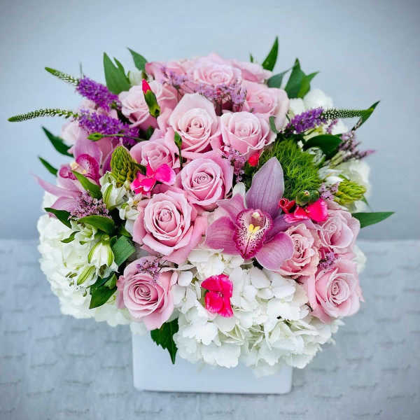 Pink roses and orchids arranged in a white square vase