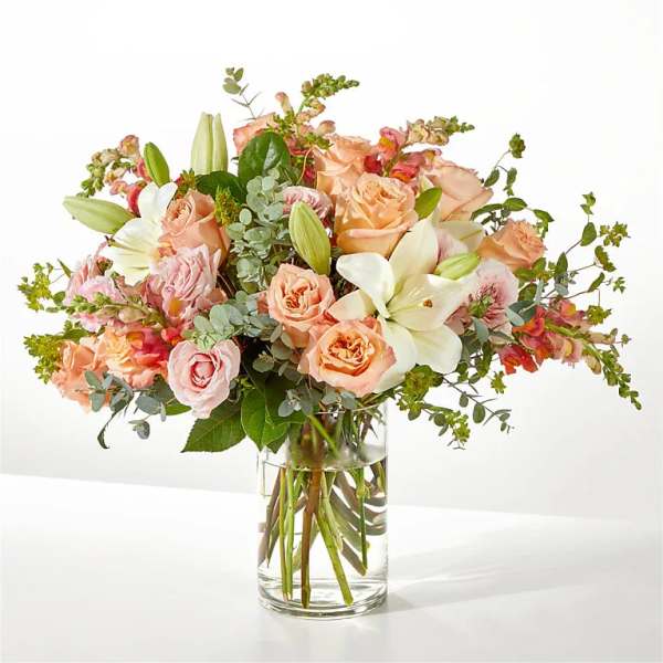Peach and pink roses with white lilies in a clear glass vase