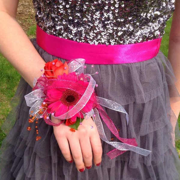Pink floral wrist corsage with ribbon on a person’s hand