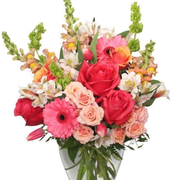 Mixed bouquet of pink roses, gerbera daisies, and peach spray roses in a clear glass vase