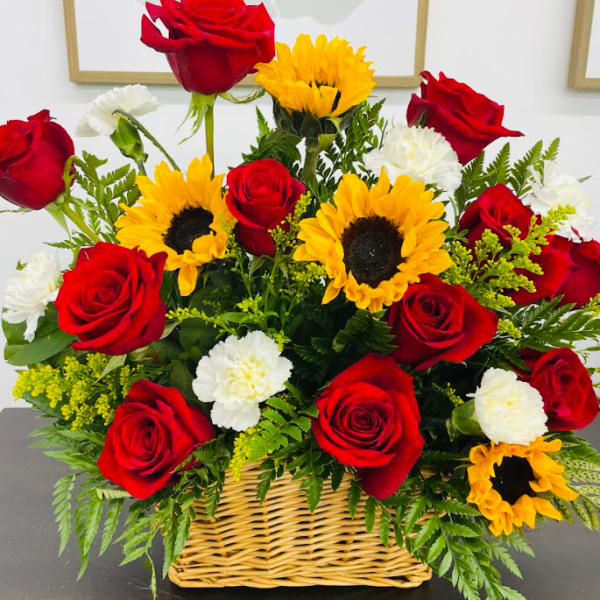 Basket arrangement of red roses, sunflowers, and white carnations