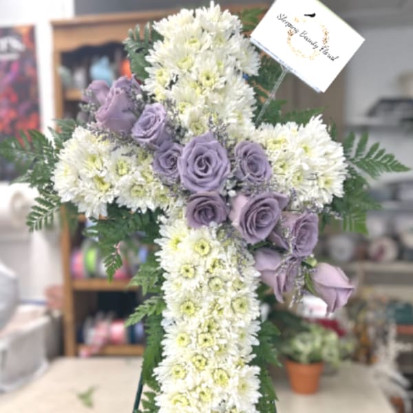 Standing white floral cross with lavender roses on an easel and a sympathy card at the top
