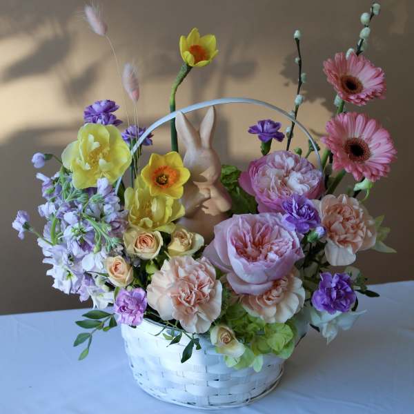 Basket arrangement with pink and yellow flowers and a small bunny figurine
