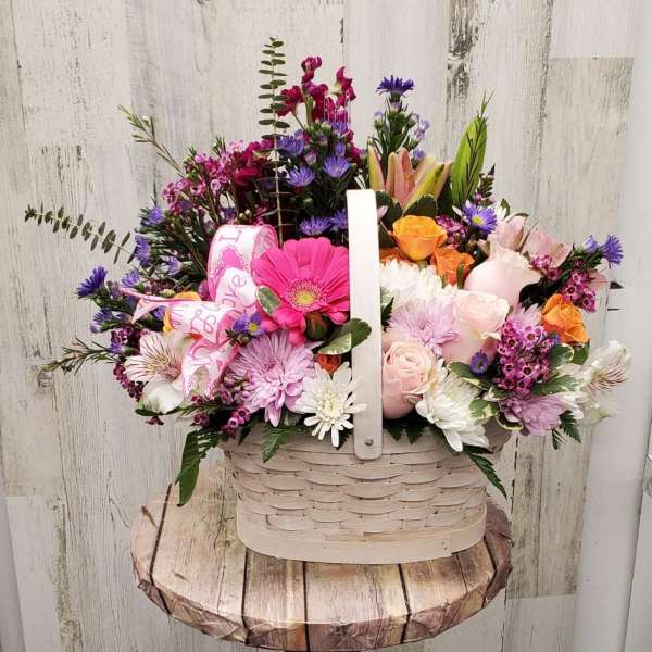 Mixed pink, purple, white, and orange flowers in a white basket on a pedestal stand